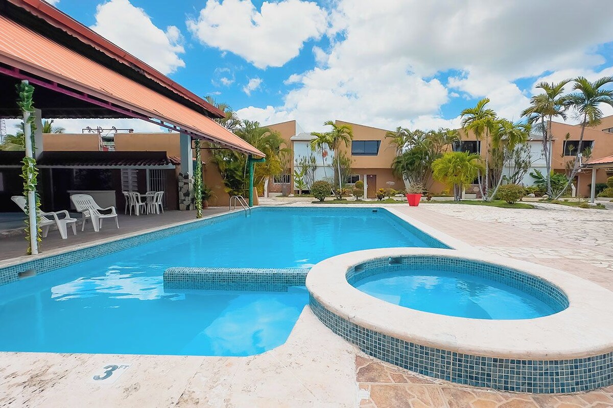 A swimming pool with a hot tub, surrounded by palm trees and a covered patio area.