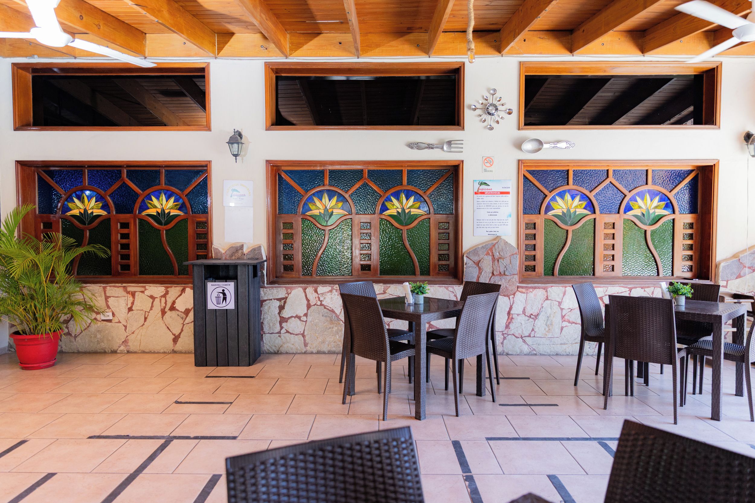 Zona pranzo all'aperto con tavoli e sedie in legno, vetrate decorative in vetro colorato e un muro in pietra.