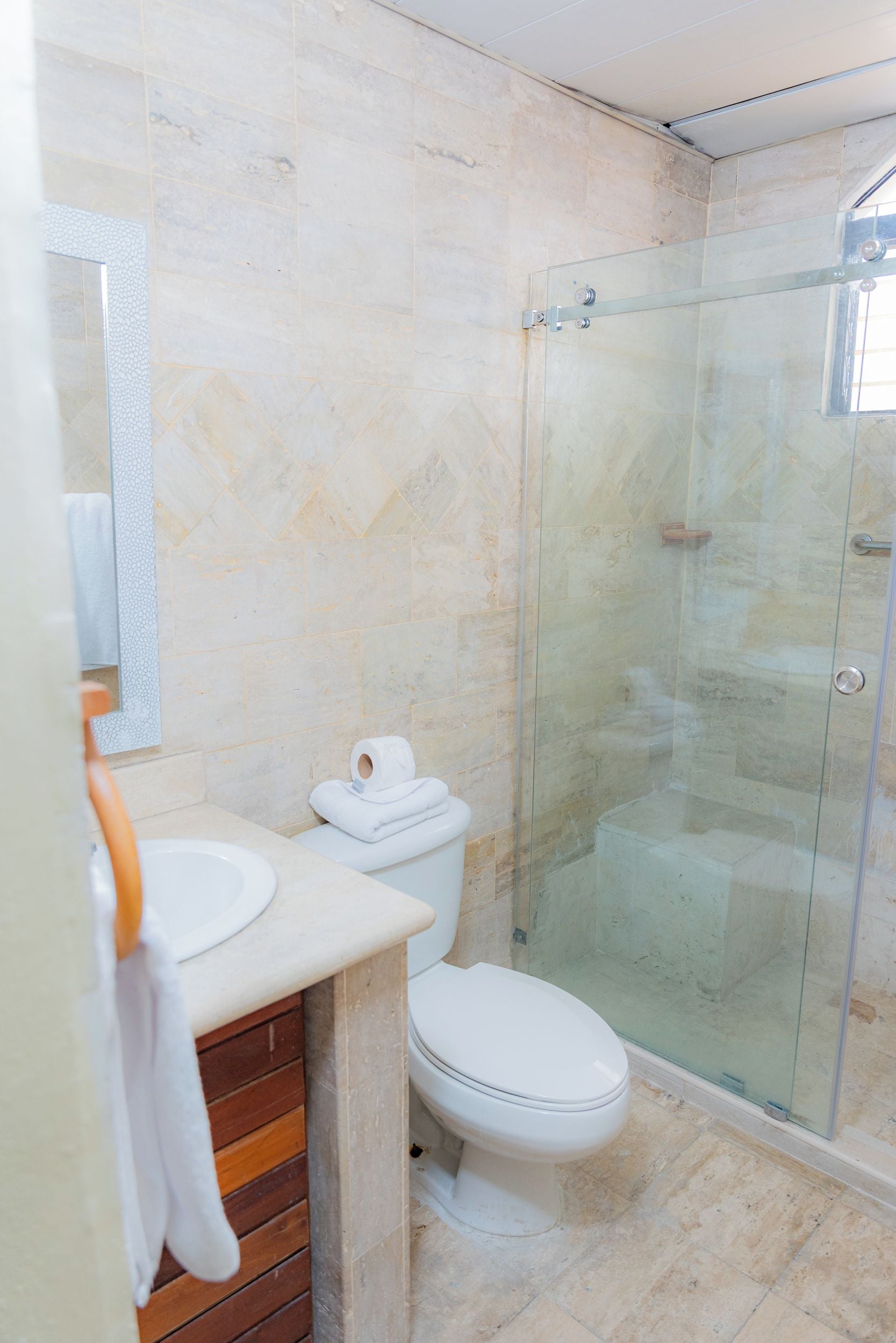 Une salle de bain moderne avec une douche à parois de verre, des toilettes blanches et un mur recouvert de carreaux de marbre.