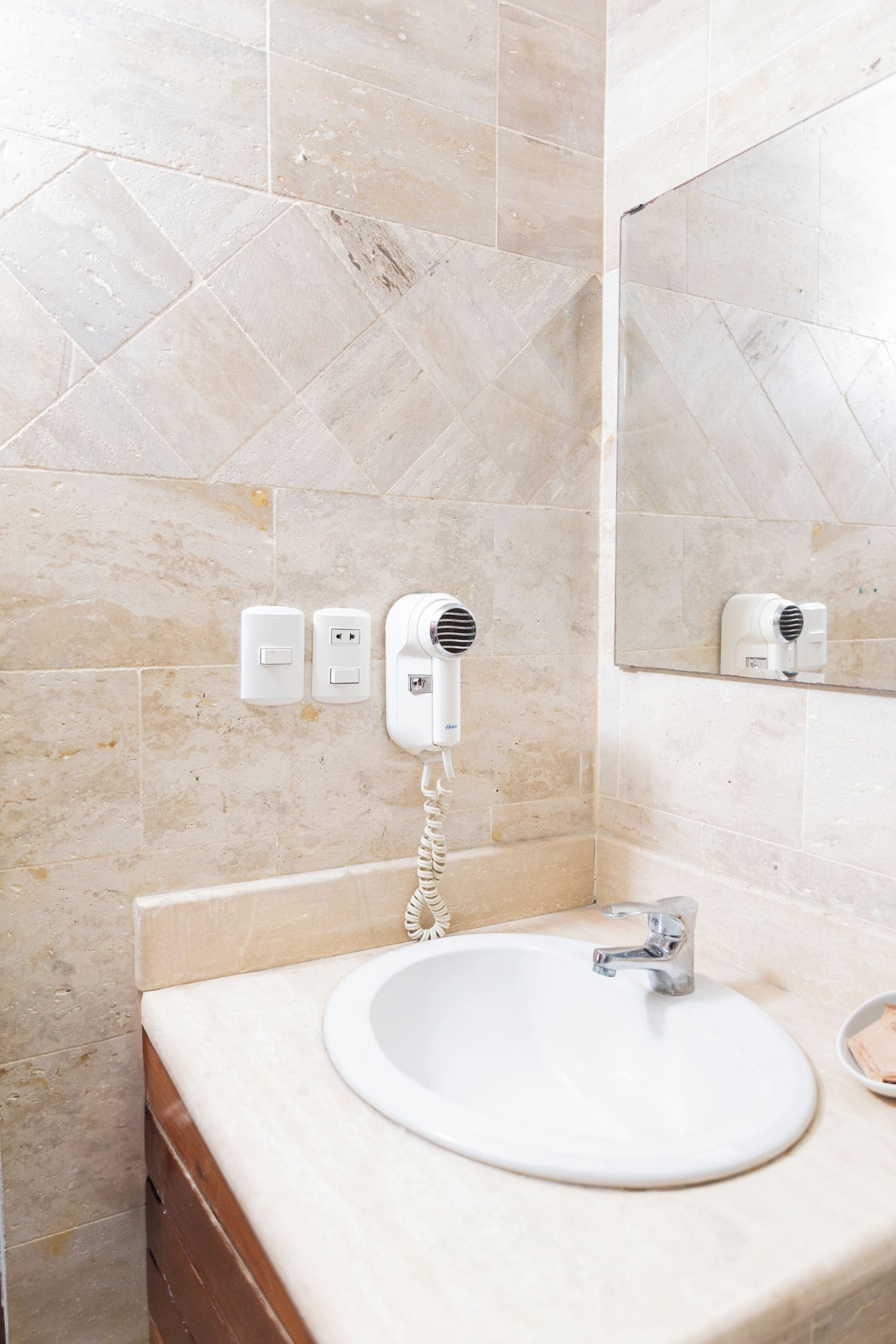 A bathroom with a white sink, a mirror, and two hair dryers mounted on the wall.