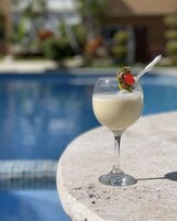 Un vaso de cóctel con cereza sobre una mesa junto a la piscina.