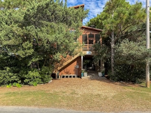 A two-story wooden building with a covered entrance and a staircase leading to the upper level. - WV64: Game Changer | Pet-friendly | Screened Porch (Ocracoke)