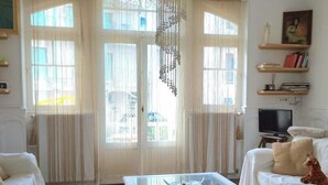 Un soggiorno con un divano bianco, un tavolino in vetro con libri, una televisione e un lampadario.