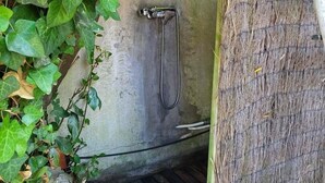 Piccola doccia chiusa con un tubo in metallo, circondata da fitta vegetazione verde.