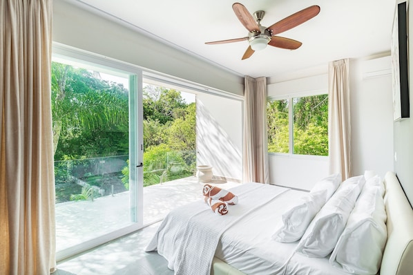 Ein Schlafzimmer mit einer großen Glasschiebetür, die zu einem Balkon führt, einem Deckenventilator und einem Bett mit weißer Bettwäsche.