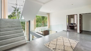 A modern interior with a marble staircase, a glass railing, and a view of greenery outside. - Villa Deluxe SlowLiving Tulum CountryClub Golf PGA (Gran Bahía Príncipe)