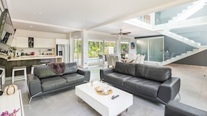 A spacious living area with two black leather sofas, a white coffee table, and a kitchen in the background. - Villa Deluxe SlowLiving Tulum CountryClub Golf PGA (Gran Bahía Príncipe)