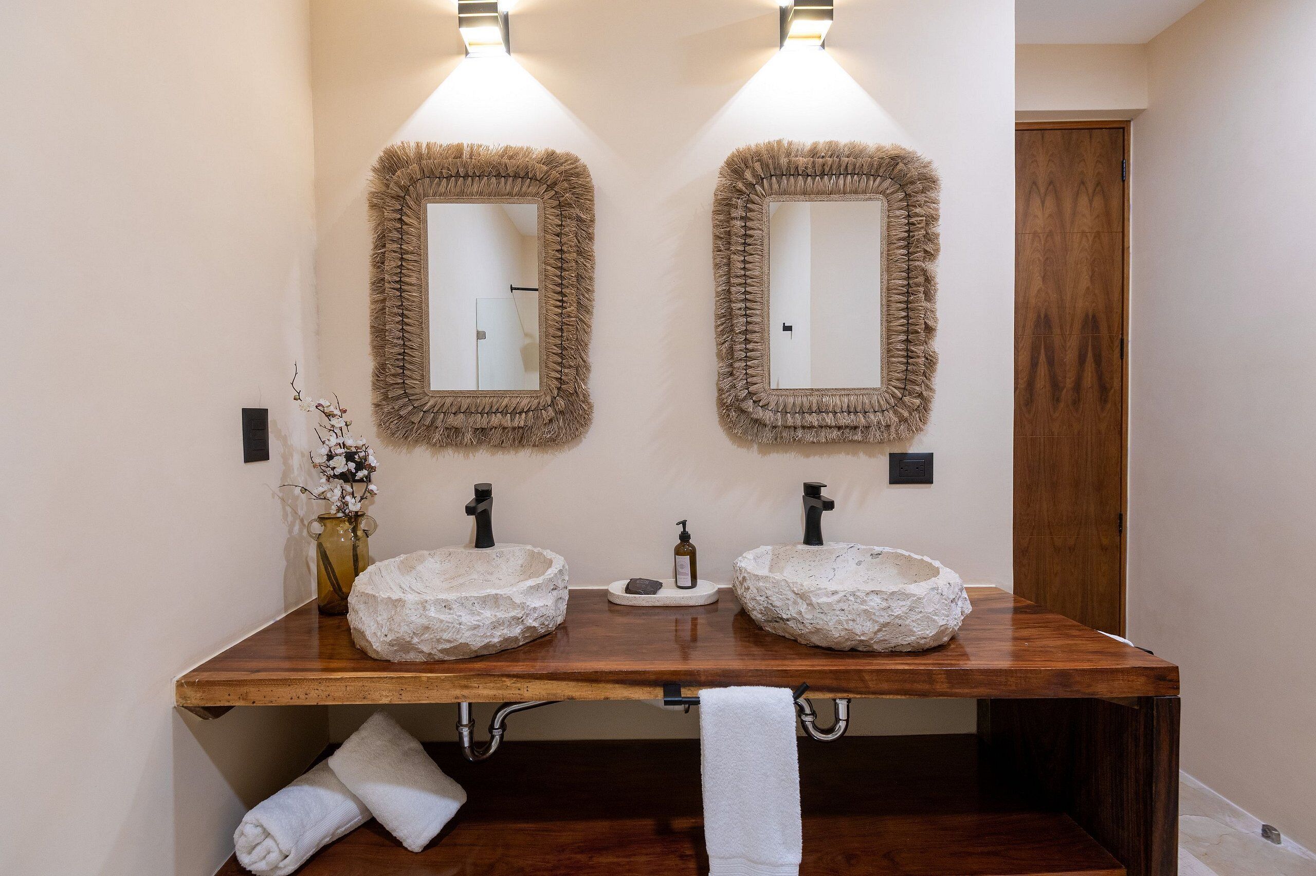 A bathroom with two stone sinks, wooden vanity, and two wall-mounted mirrors with fluffy frames.