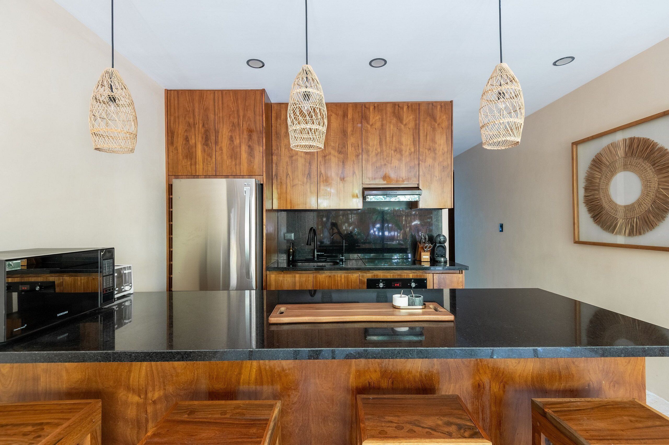 A modern kitchen with wooden cabinets, stainless steel appliances, a black countertop, and three woven pendant lights.