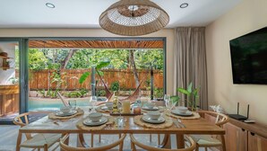 A dining area with a table set for six, a large woven pendant light, and a view of a swimming pool and garden. - •LUMA SwimUp Pools, Garden & Quiet Living | Tulum (Tulum)