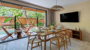 A dining area with a wooden table, chairs, and a TV mounted on the wall. - •LUMA SwimUp Pools, Garden & Quiet Living | Tulum (Tulum)
