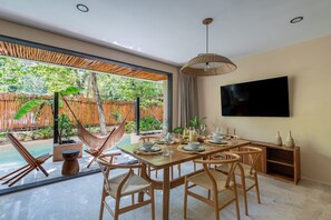A dining area with a wooden table, chairs, and a TV mounted on the wall. - •LUMA SwimUp Pools, Garden & Quiet Living | Tulum (Tulum)