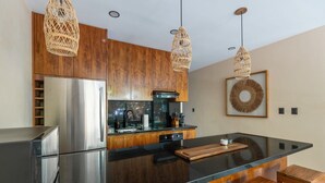 A modern kitchen with wooden cabinets, stainless steel appliances, and a black granite countertop. - •LUMA SwimUp Pools, Garden & Quiet Living | Tulum (Tulum)