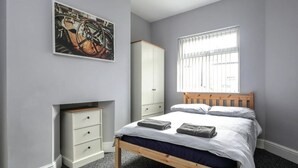 A bedroom with a wooden bed, a white wardrobe, a nightstand, and a window with blinds. - 5 bedroom house, free parking, near football, sleeps 8 (Liverpool)