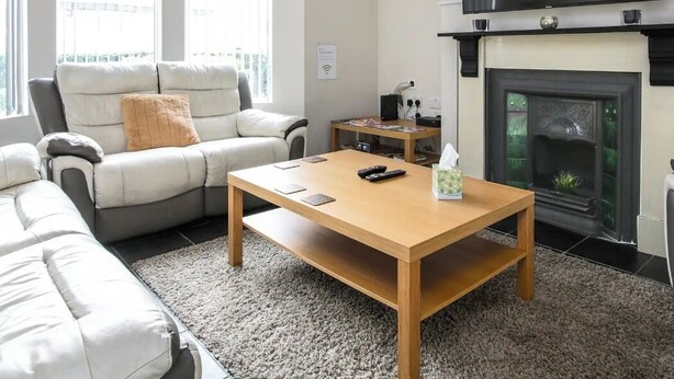 A living room with a sofa, a coffee table, a fireplace, and a TV mounted on the wall. - 5 bedroom house, free parking, near football, sleeps 8 (Liverpool)