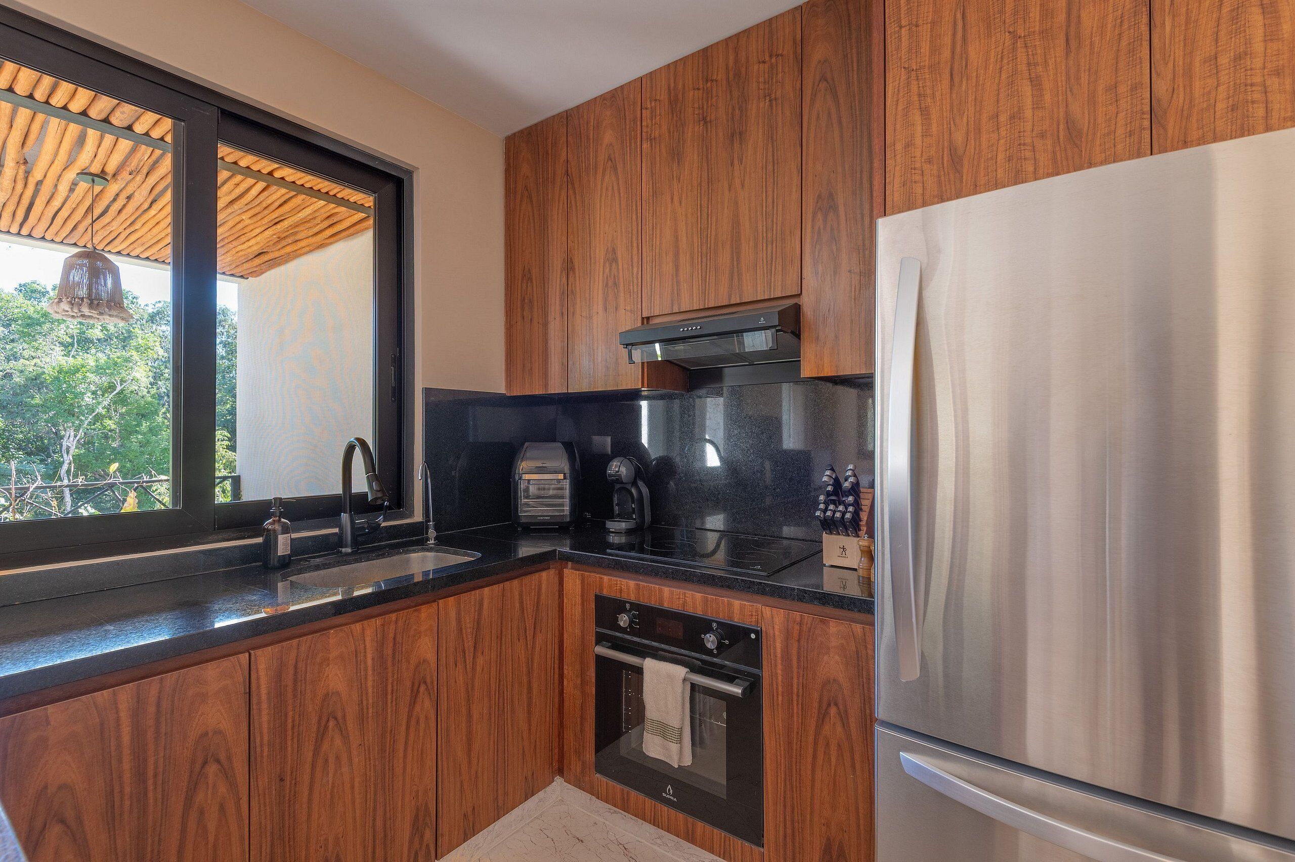 A modern kitchen with wooden cabinets, a stainless steel refrigerator, a built-in oven, and a coffee maker.