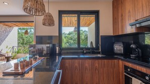 A modern kitchen with wooden cabinets, a black countertop, and a large window with a view of greenery. - •|AMARU Penthouse | Private Rooftop & Quiet Living (Tulum)
