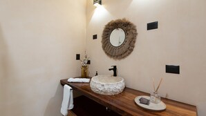 A bathroom with a wooden vanity, a round mirror with a fur-like frame, a stone sink, a towel, and a small vase with reeds. - •|AMARU Penthouse | Private Rooftop & Quiet Living (Tulum)