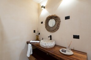 A bathroom with a wooden vanity, a round mirror with a fur-like frame, a stone sink, a towel, and a small vase with reeds. - •|AMARU Penthouse | Private Rooftop & Quiet Living (Tulum)