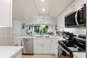 A modern kitchen with white cabinetry, a built-in microwave, and a dishwasher. - B-114 -Totally Remodeled With Walk Out Lanai (Naples)