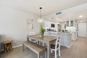 A modern kitchen with white cabinets, a central island, and a dining area with a wooden table and chairs. - B-114 -Totally Remodeled With Walk Out Lanai (Naples)