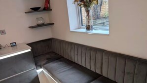 A modern kitchen with a built-in bench, a window with a view, and a small shelf with decorative items.