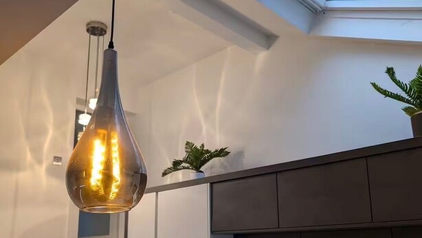 A modern kitchen with a skylight, a hanging light fixture, and a staircase.