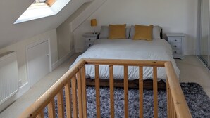 A bedroom with a sloped ceiling, a skylight, a bed with white bedding, wooden headboard, and a small bedside table with a lamp.