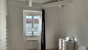 A room with a large window, a radiator, a white dresser, and a chair. - Luxembourg Montparnasse (Paris)