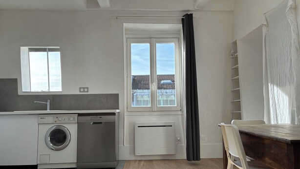 A compact kitchen with a washing machine, a built-in oven, and a window with curtains. - Luxembourg Montparnasse (Paris)