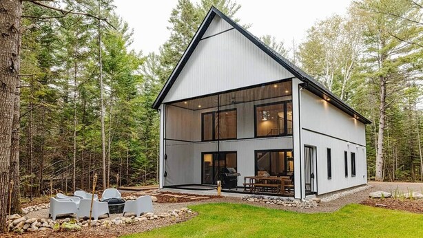 Ein modernes, zweistöckiges Haus mit großer Glasfront, umgeben von einem Wald.