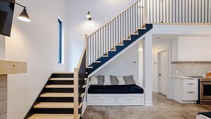 Ein modernes Interieur mit einer Treppe, die zu einem Schlafzimmer auf dem Dach führt, einer Küchenzeile und einem sichtbaren Fenster.