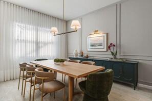 Ruokailutilassa on puinen pöytä, kuusi tuolia, vihreäverhoiltu tuoli, tummansininen kaappi ja seinällä oleva kehystetty taulu.