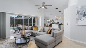 A modern living room with a sectional sofa, a dining area, and a kitchen. - Lely Resort Single-Family Home Monthly Min Stay (Naples)