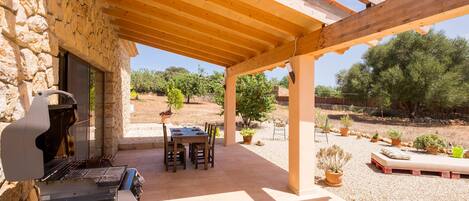 Un patio cubierto con pared de piedra, una parrilla, una mesa con sillas y plantas en macetas.