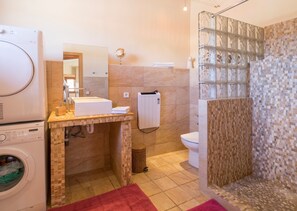 Ein Badezimmer mit Waschmaschine, Toilette, einer Dusche mit Mosaikfliesen und einem Handtuchhalter.