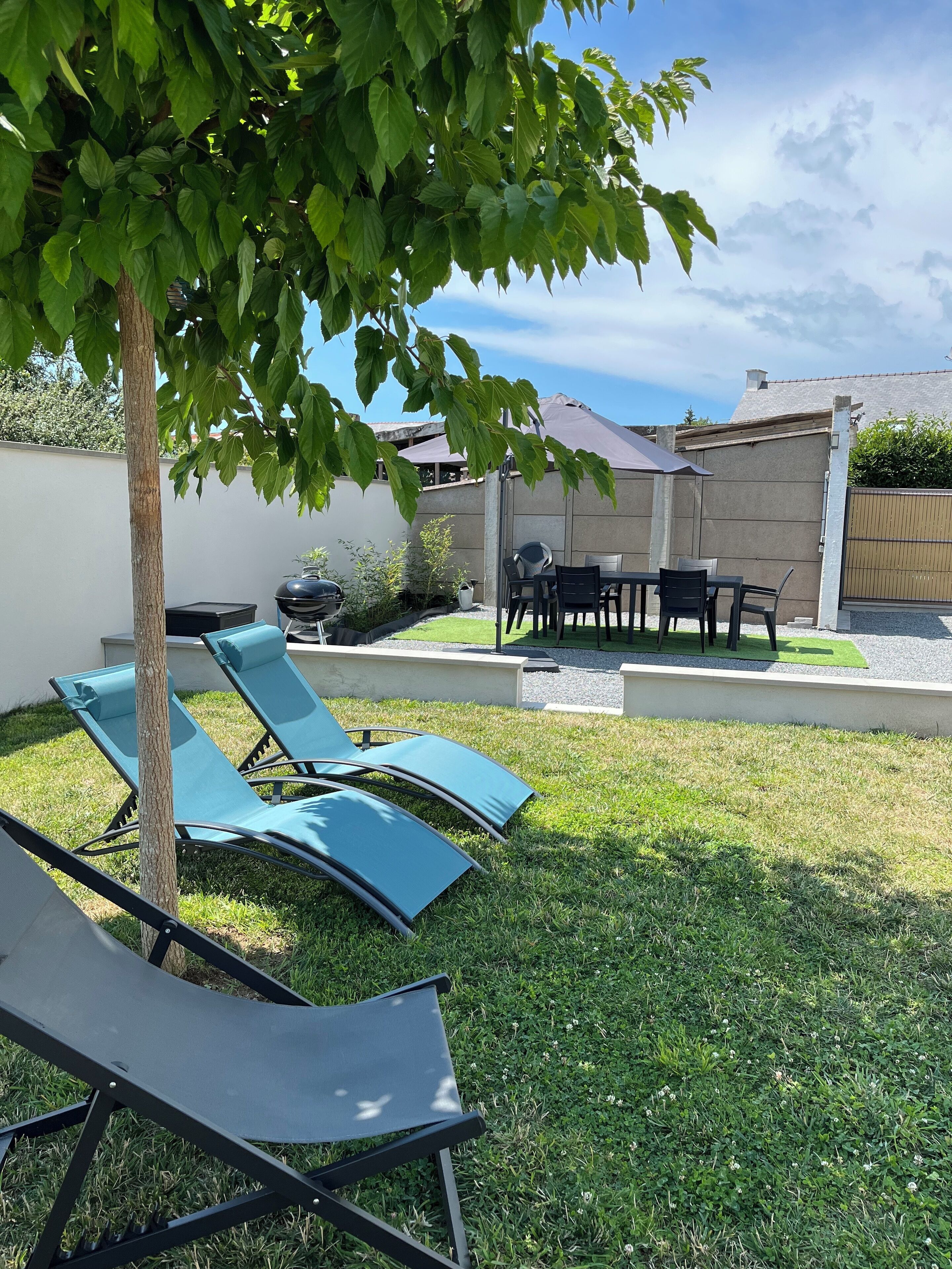 A backyard with a lawn, a barbecue grill, and a table with chairs.