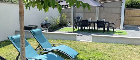 A backyard with a lawn, a barbecue grill, and a table with chairs.