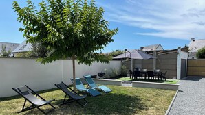Patio trasero con un árbol, una parrilla y mobiliario exterior.