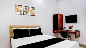 Hotellihuone, jossa on sänky, työpöytä, tuoli, televisio ja kolme kehystettyä taideteosta seinällä.