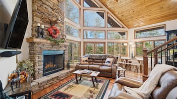 A spacious living room with a stone fireplace, leather furniture, and large windows offering a view of the outdoors.