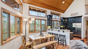 A spacious kitchen with wooden cabinetry, a central island with stools, and large windows offering a view of the outdoors.