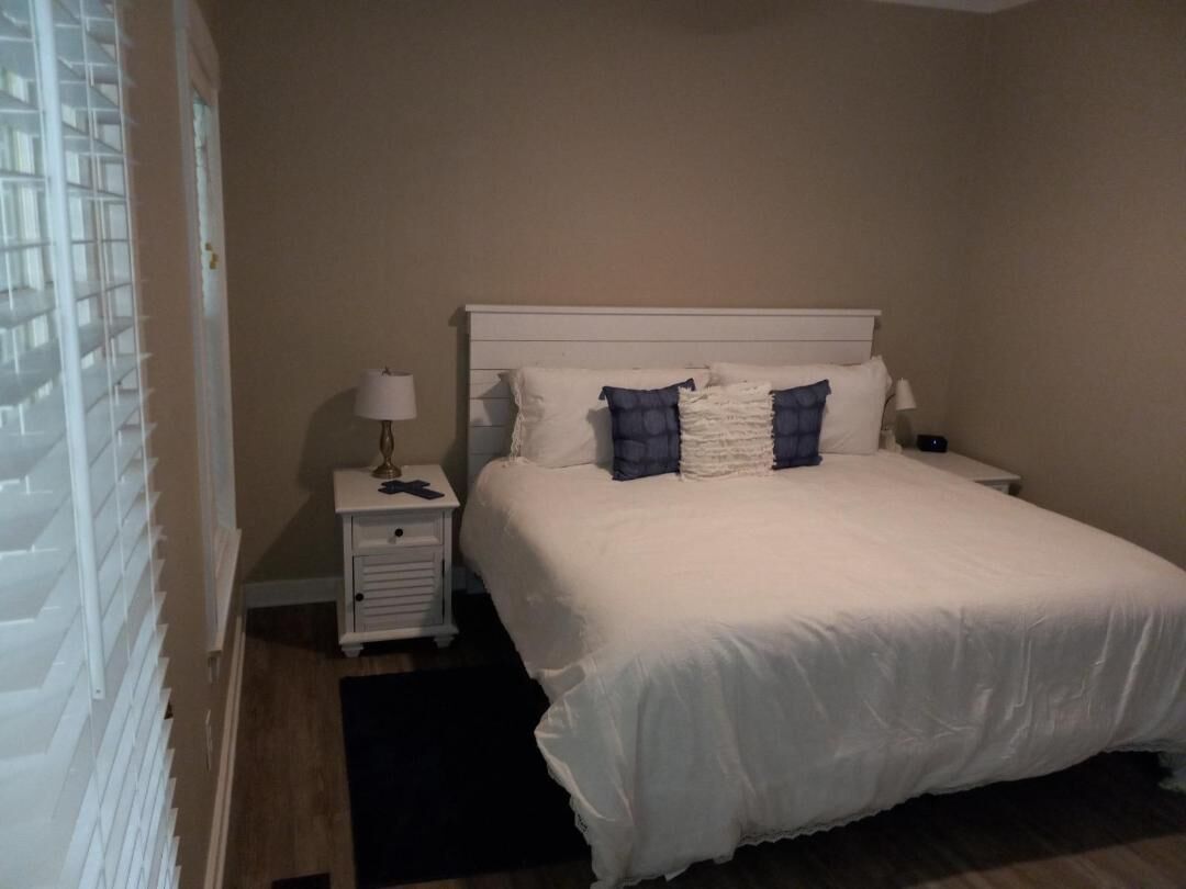A bedroom with a large bed, a nightstand with a lamp, and a small drawer unit.