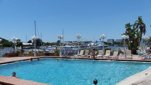 Una piscina con sillones de descanso y vista a barcos al fondo.