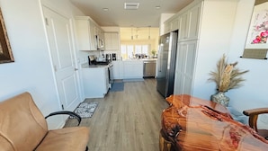A modern kitchen with white cabinets, stainless steel appliances, and a wooden dining table. -  Sun-Filled Brand-New Edenfield Designer Home (Sumterville)