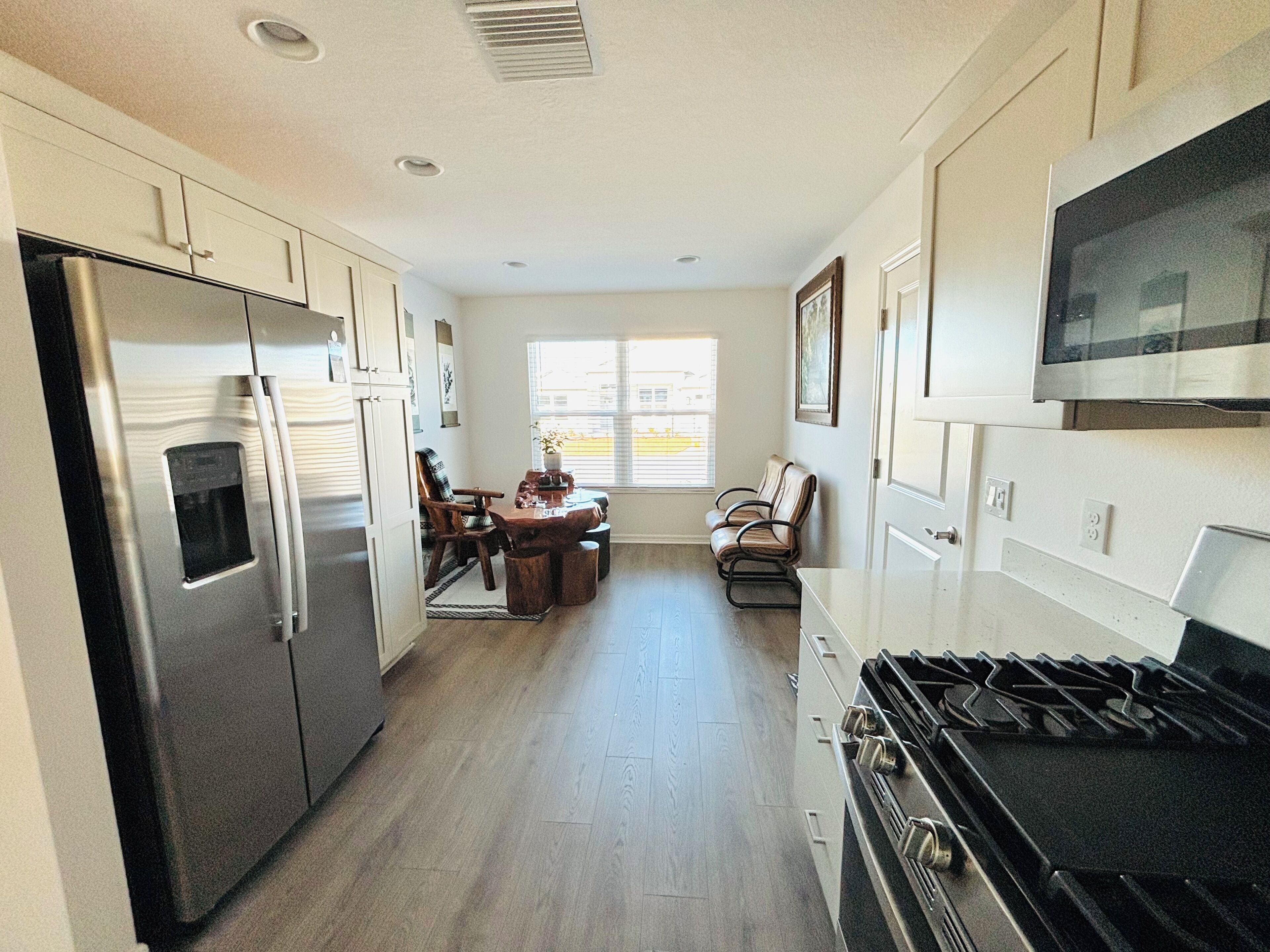 Una cocina equipada con refrigerador, estufa, microondas, mesa de comedor con sillas y una ventana con persianas.