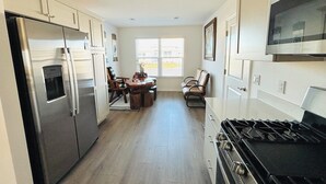 A kitchen with a refrigerator, stove, microwave, dining table with chairs, and a window with blinds. -  Sun-Filled Brand-New Edenfield Designer Home (Sumterville)