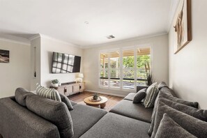 Una sala de estar moderna con un sofá seccional gris, una mesa de centro y un televisor montado en la pared.