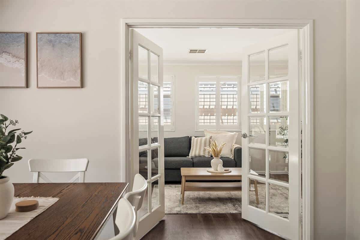 A room with a dining table, chairs, a sofa, a coffee table, and a door leading to another room.