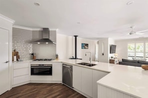 Une cuisine moderne avec des meubles blancs, un lave-vaisselle, une cuisinière et une hotte noire.